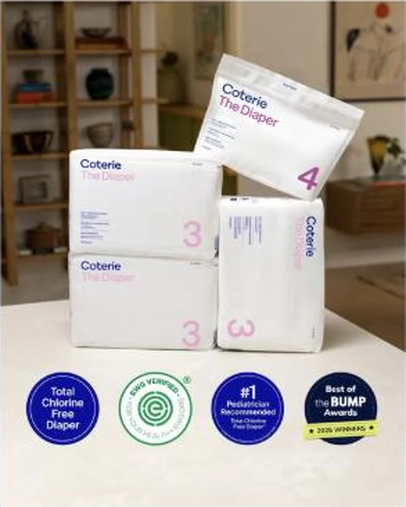 Four award badges over a living-room stack of diaper packs